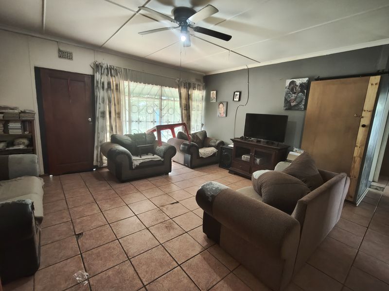 A living room featuring tiled flooring, a ceiling fan, and a sliding door with security gate, requiring cosmetic updates to improve the overall condition.