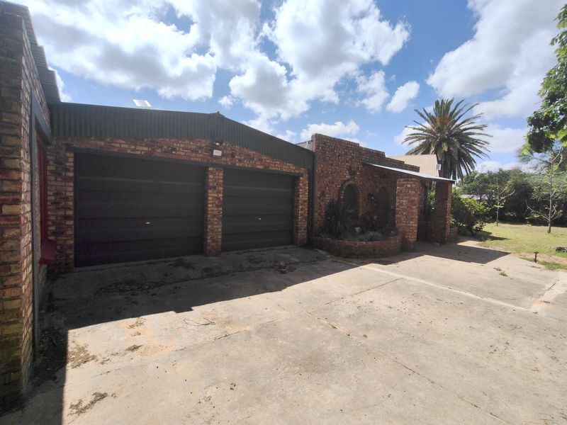 Front exterior view of a brick house featuring a double garage, concrete driveway, and a covered entrance area with a built-in brick planter.