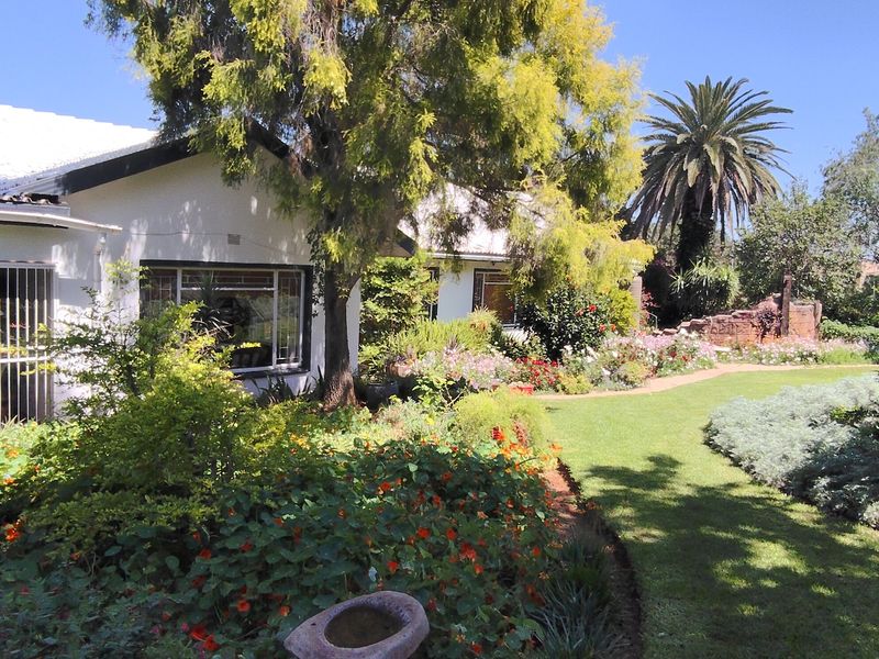 A well-maintained rear garden featuring a lush lawn, mature trees, and vibrant flower beds adjacent to the house exterior.