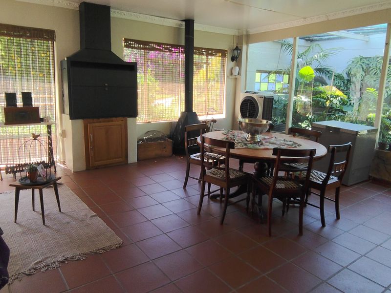 Spacious enclosed patio featuring tiled flooring and a built-in braai, offering a versatile indoor-outdoor entertainment area with garden views.