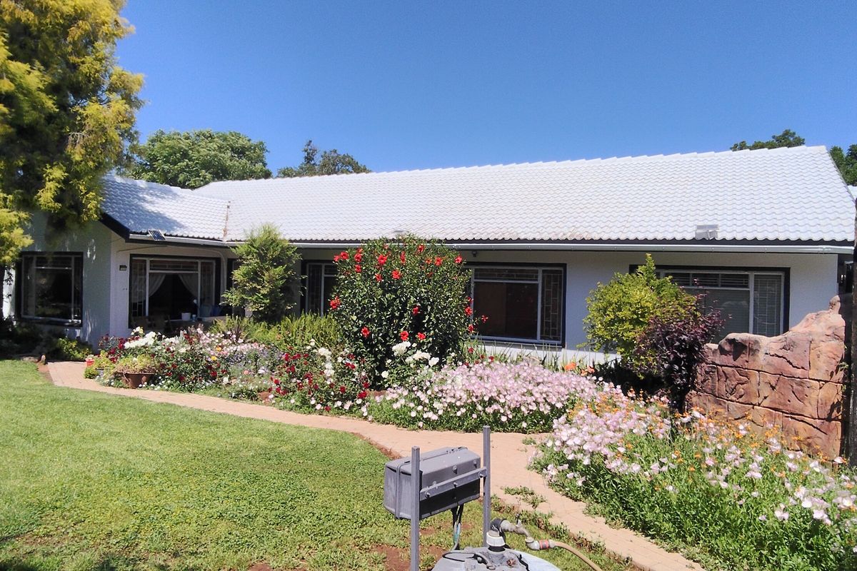 A well-maintained rear exterior view of the house featuring a tiled roof, stone feature wall, and a lush, landscaped garden with a paved walkway.