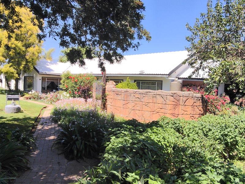 A view of the rear garden featuring a brick pathway, established landscaping, and a stone retaining wall leading to the main house structure.