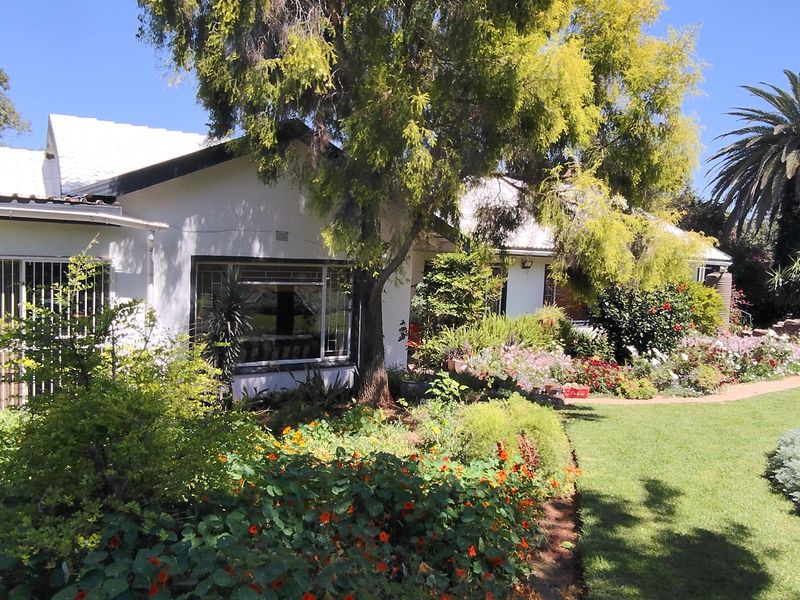 A well-maintained rear garden featuring a lush lawn, mature trees, vibrant flower beds, and a paved pathway leading to the house exterior.