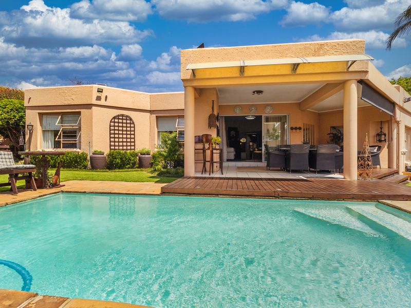 A well-maintained outdoor entertainment area featuring a swimming pool, timber decking, and a covered patio with direct access to the home's interior.