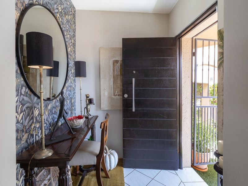 Welcoming entrance hall featuring tiled flooring, a solid timber front door, and a security gate, accented by decorative wallpaper.