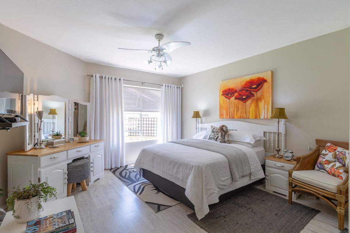 A well-maintained bedroom featuring light-toned laminate flooring, a central ceiling fan, and natural light through a window with curtains.