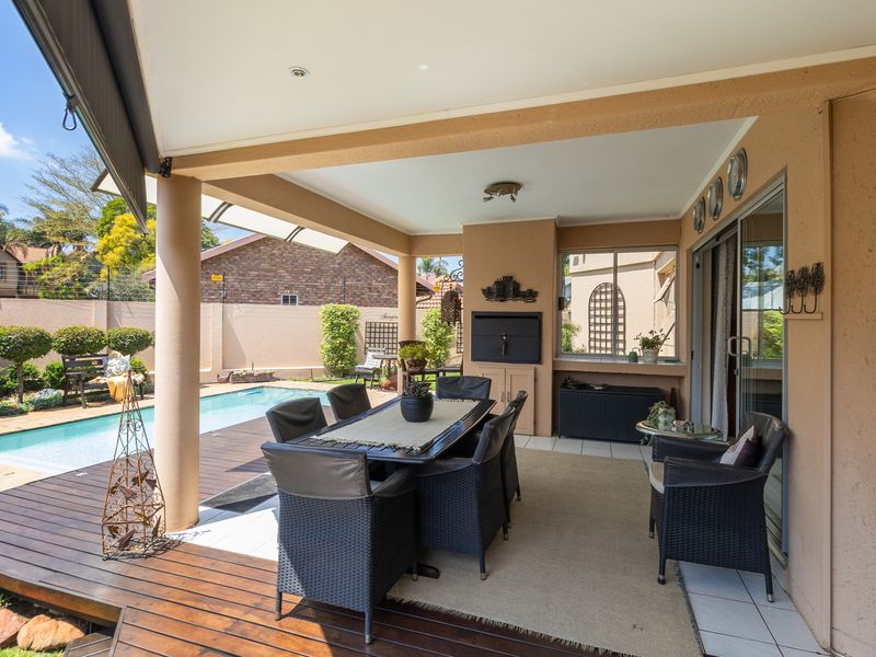 A spacious covered patio featuring wooden decking, a built-in braai, and direct access to the swimming pool area, perfect for outdoor entertaining.