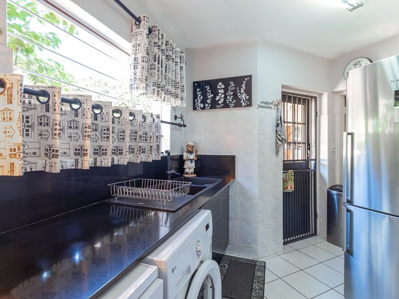 Functional scullery area featuring black granite countertops, an undermount sink, tiled backsplash, and a secure rear access door.