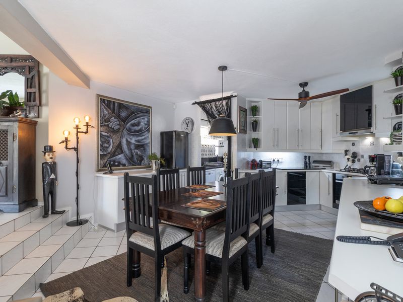 Open-plan kitchen and dining area featuring tiled flooring, white cabinetry, built-in appliances, and a raised platform area with decorative tiling.