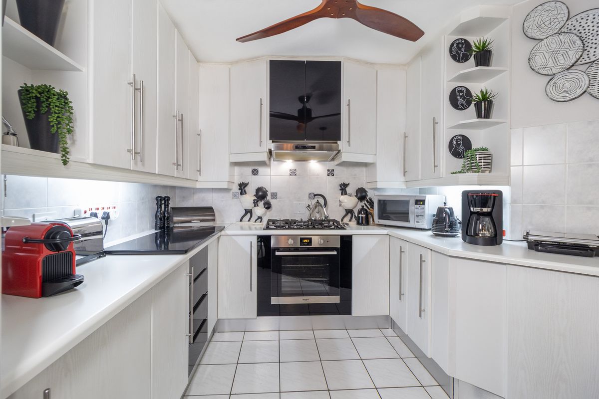 A well-maintained galley kitchen featuring white cabinetry, a gas hob, built-in oven, extractor fan, and tiled flooring with integrated under-cabinet lighting.
