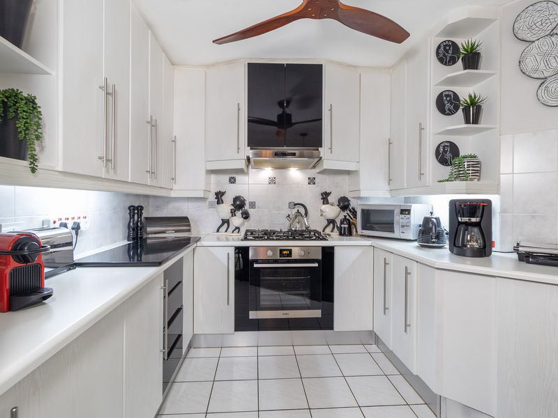 A well-maintained galley kitchen featuring white cabinetry, a gas hob, built-in oven, extractor fan, and tiled flooring with integrated under-cabinet lighting.