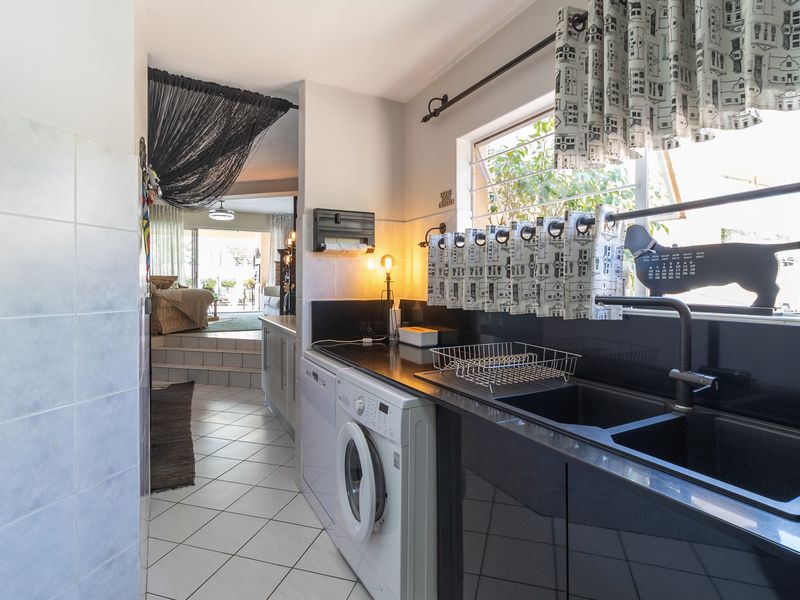 Functional scullery area featuring dark cabinetry, granite countertops, double basin sink, and tiled finishes, providing convenient access to the adjacent living space.