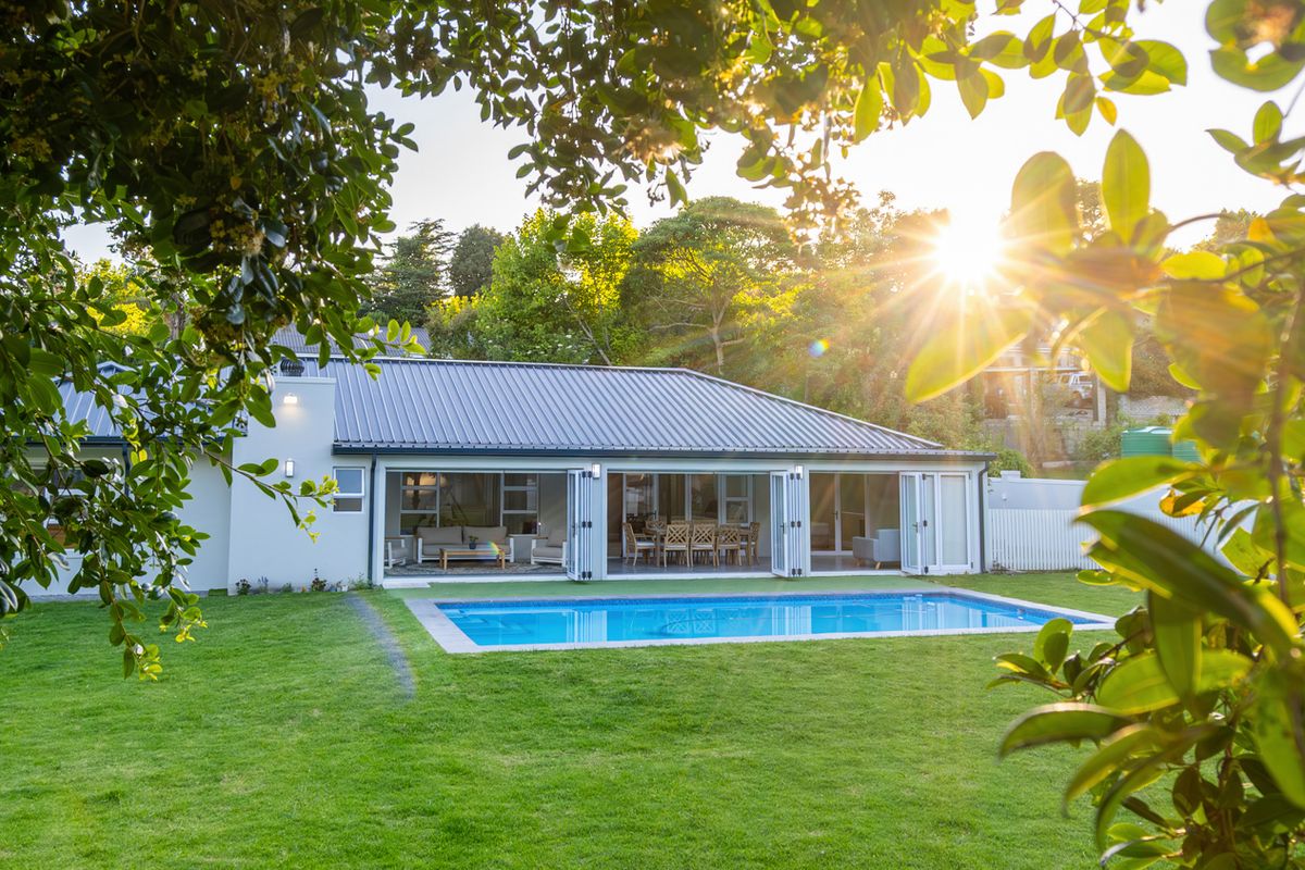 A well-maintained rear exterior view featuring a swimming pool, manicured lawn, and large folding glass doors opening into the home.