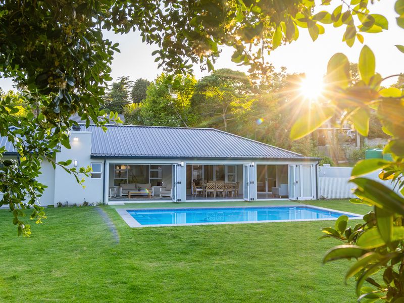A well-maintained rear exterior view featuring a swimming pool, manicured lawn, and large folding glass doors opening into the home.