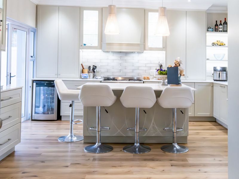 Modern kitchen featuring a central island with breakfast bar seating, high-end cabinetry, subway tile backsplash, integrated wine cooler, and premium hardwood flooring.