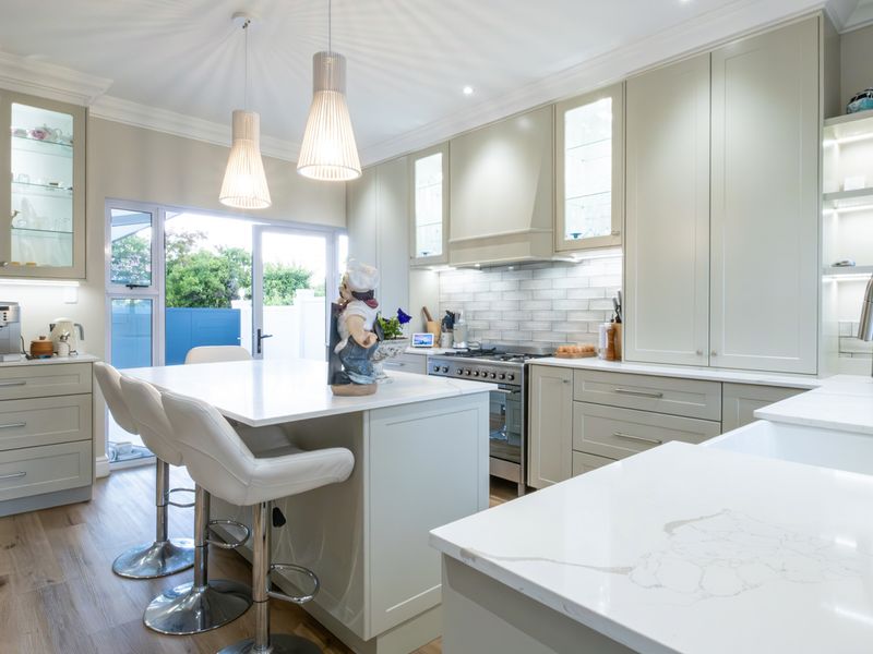 Modern kitchen featuring high-end shaker cabinetry, quartz countertops, a central island, gas stove, and elegant pendant lighting with direct access to the outdoor area.