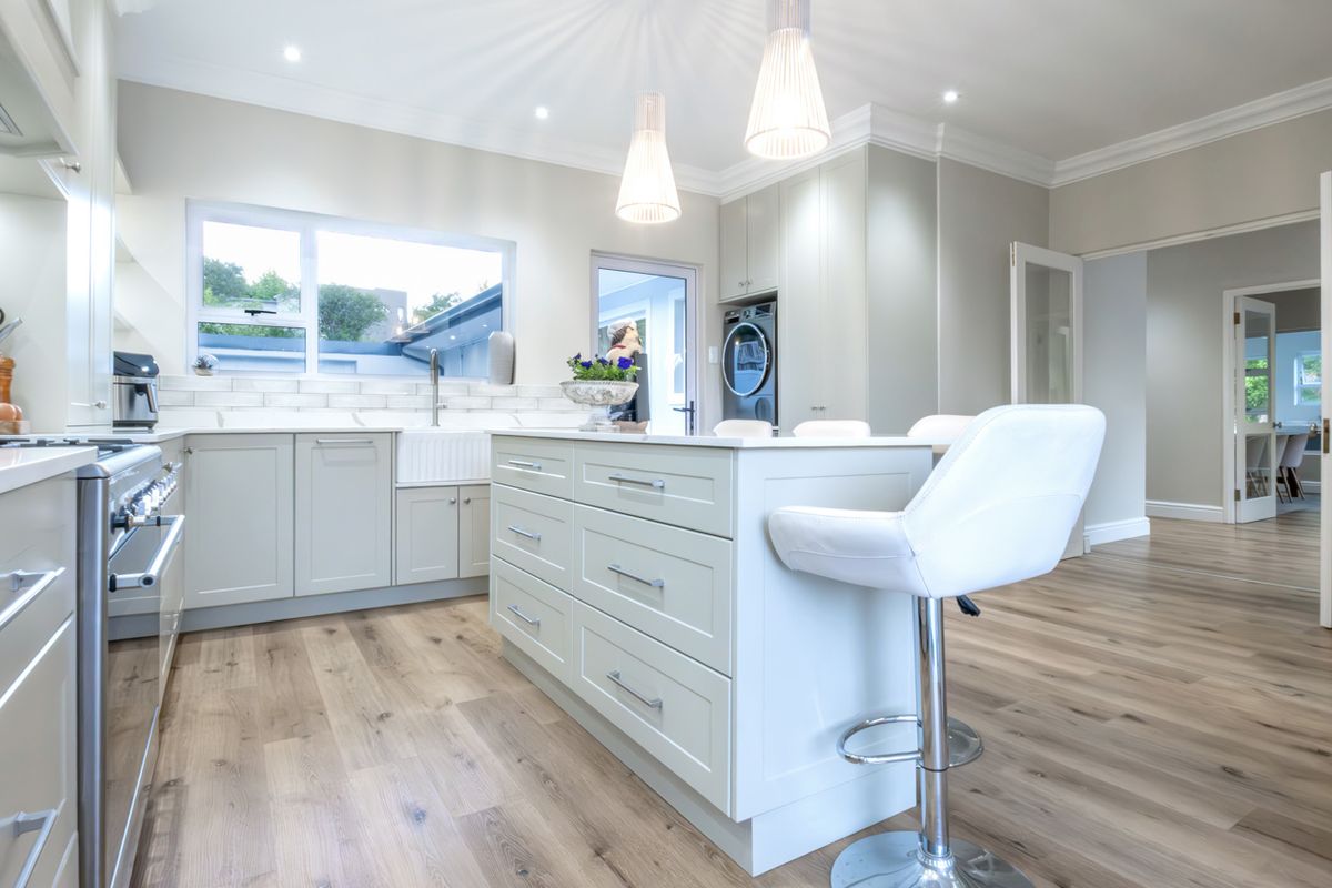 Modern kitchen featuring a central island, shaker-style cabinetry, apron-front sink, and high-end gas range, finished with light wood-look flooring and recessed lighting.