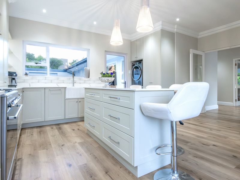 Modern kitchen featuring a central island, shaker-style cabinetry, apron-front sink, and high-end gas range, finished with light wood-look flooring and recessed lighting.