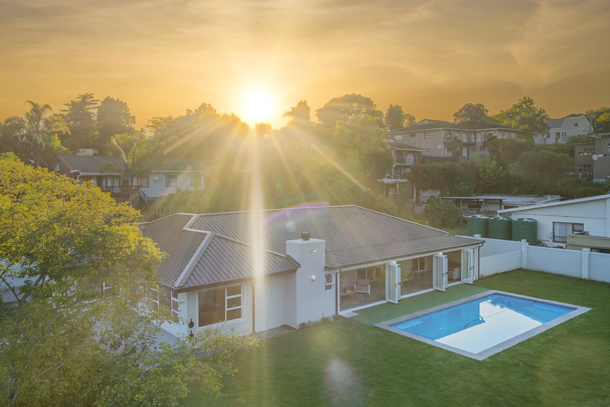 Aerial view of a residential property featuring a swimming pool, manicured lawn, metal roof, and bi-fold doors opening to the outdoor area at sunset.