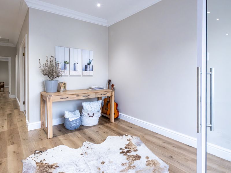 A bright and modern hallway featuring high-quality timber flooring, recessed downlighting, and clean neutral wall finishes with elegant cornice detailing.
