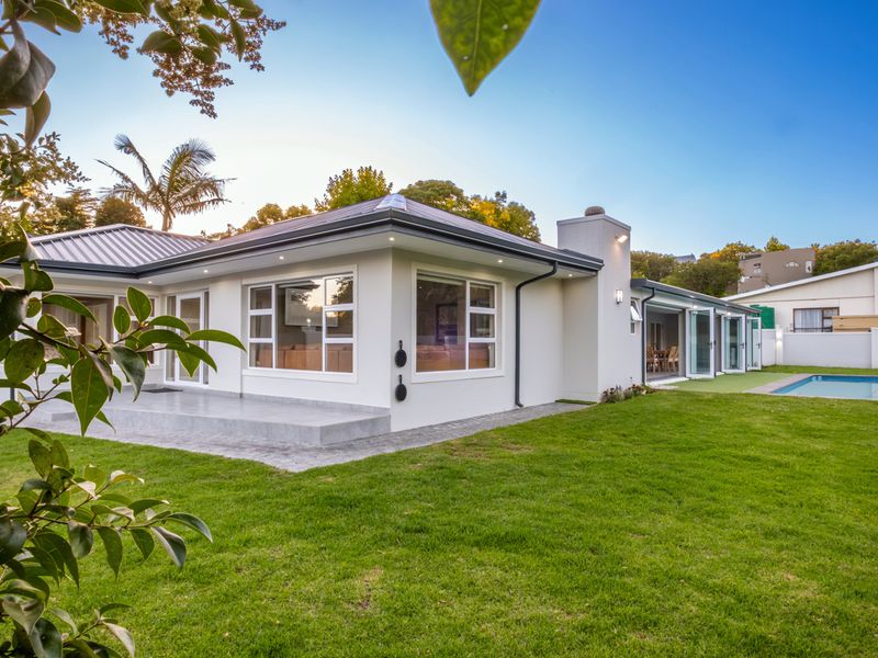 Rear view of the property featuring a well-maintained lawn, swimming pool, paved patio area, and modern bi-fold doors leading into the home.