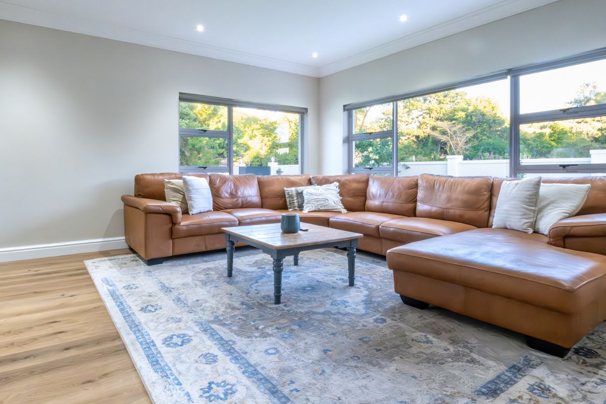 A bright and modern living room featuring laminate flooring, recessed downlights, and large aluminium-framed windows that provide ample natural light.