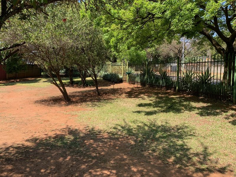 A spacious garden area featuring mature trees, established landscaping, and secure metal perimeter fencing.