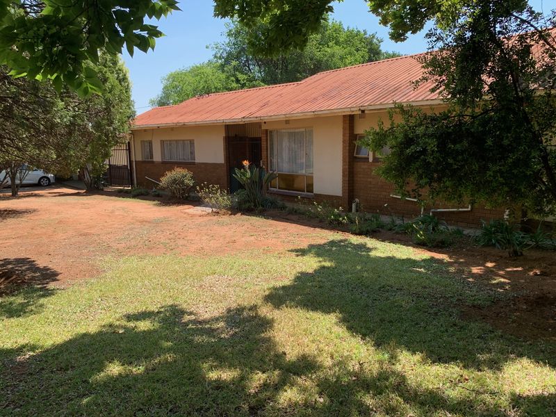 Front view of a single-story house featuring a corrugated metal roof, brick exterior walls, and a large front garden area.