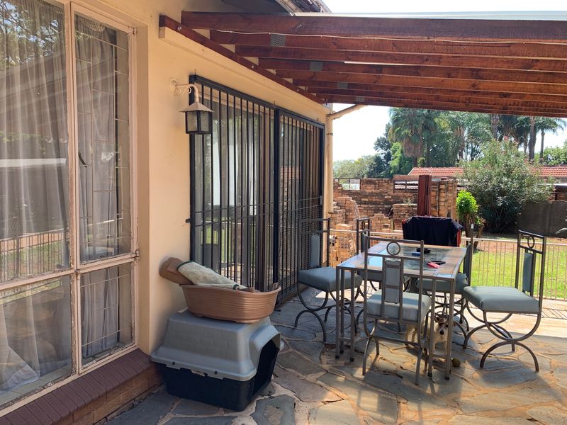 Covered outdoor patio area featuring stone paving, a timber pergola, and direct access to the garden through security gates.