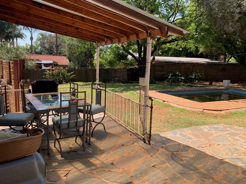 Covered outdoor patio area featuring stone paving and a timber pergola, overlooking a private garden and swimming pool.