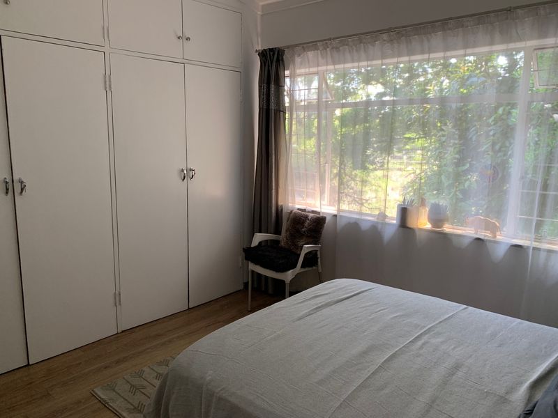 A bedroom featuring laminate flooring, large windows providing natural light, and ample built-in cupboard storage space.