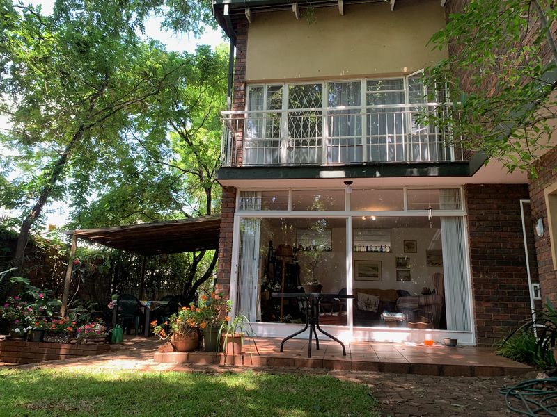 Rear view of the townhouse featuring a brick facade, a private balcony with metal railing, and a tiled patio area with a covered pergola.
