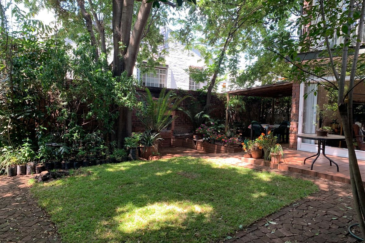 A private rear garden featuring a lawn, brick paving, raised garden beds, and a covered patio area adjacent to the townhouse.