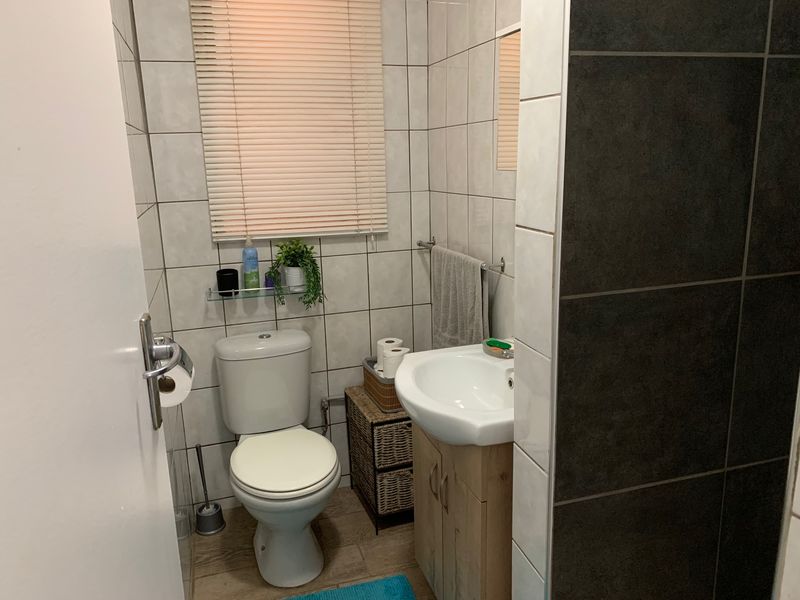 A compact bathroom featuring a toilet, vanity basin, and neutral wall tiling with a contrasting dark tiled shower area.
