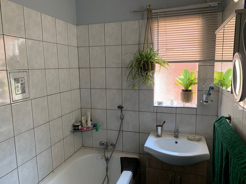 A functional bathroom featuring a bathtub with a handheld shower attachment, a vanity cabinet with a washbasin, and tiled wall finishes.