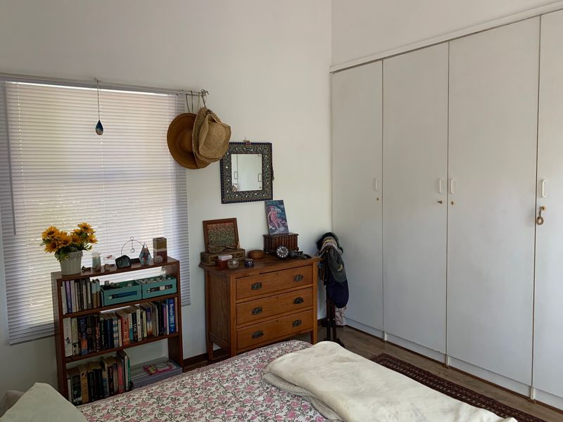 A bedroom featuring built-in cupboards, laminate flooring, and venetian blinds, offering a functional space with neutral finishes.