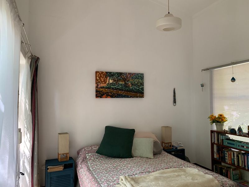 A bright bedroom featuring white walls, a pendant light fixture, and window treatments including curtain tracks and venetian blinds.