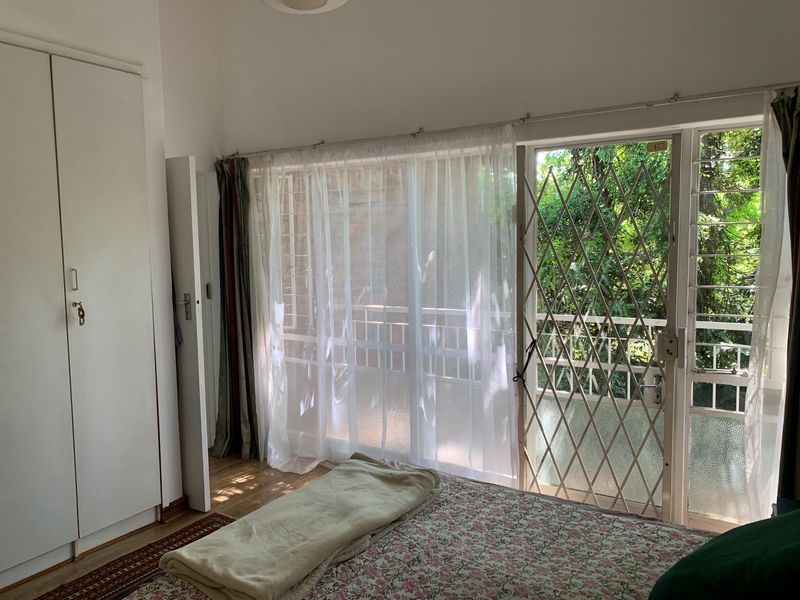 A bedroom featuring built-in cupboards, laminate flooring, and a sliding glass door with a security gate leading to an outdoor area.