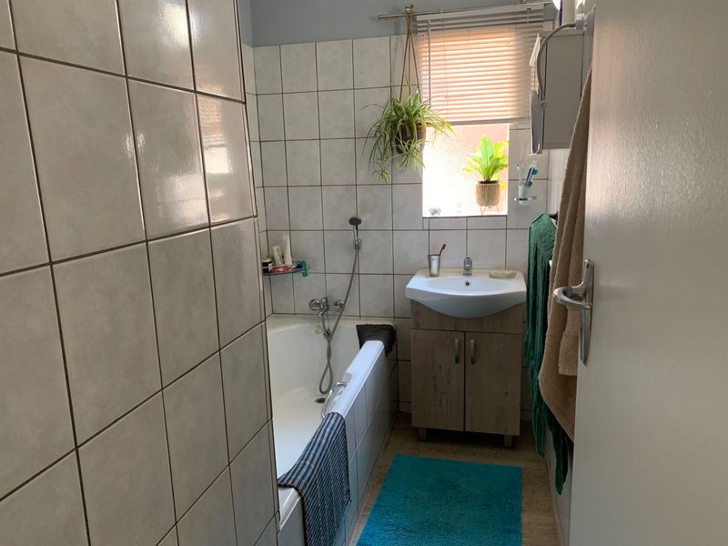 A functional bathroom featuring a built-in bathtub, a vanity cabinet with a washbasin, and tiled walls.