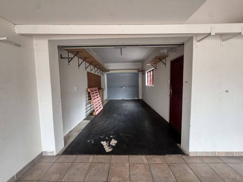 A spacious, empty garage featuring a roller shutter door, side access door, and wall-mounted shelving brackets, providing ample storage or parking space.
