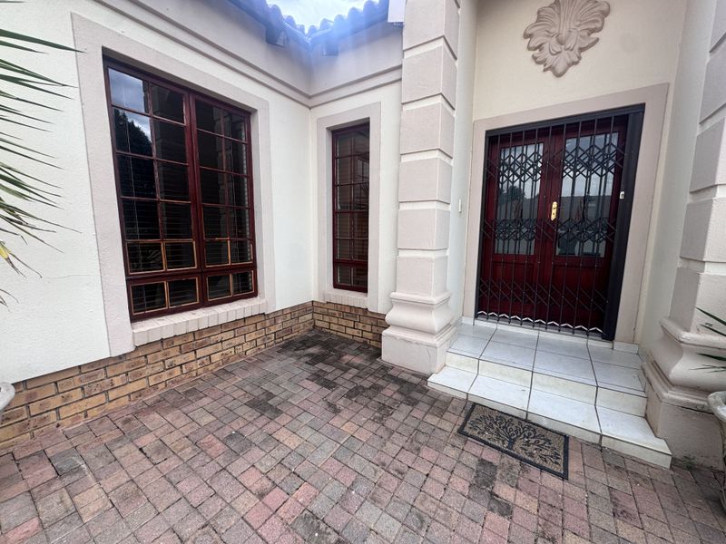 Entrance area featuring a paved courtyard, security gate, and double timber doors with decorative architectural detailing.