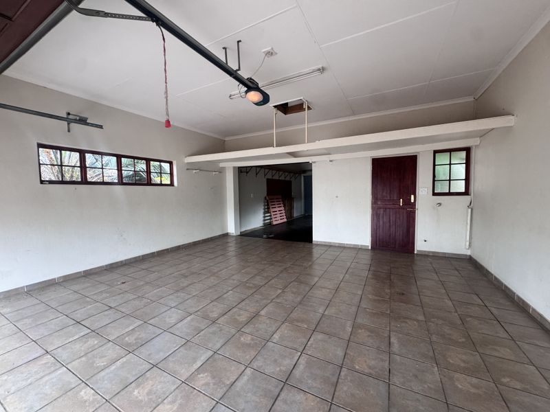 Spacious double garage featuring tiled flooring, a ceiling access hatch, and direct internal access through a timber door.