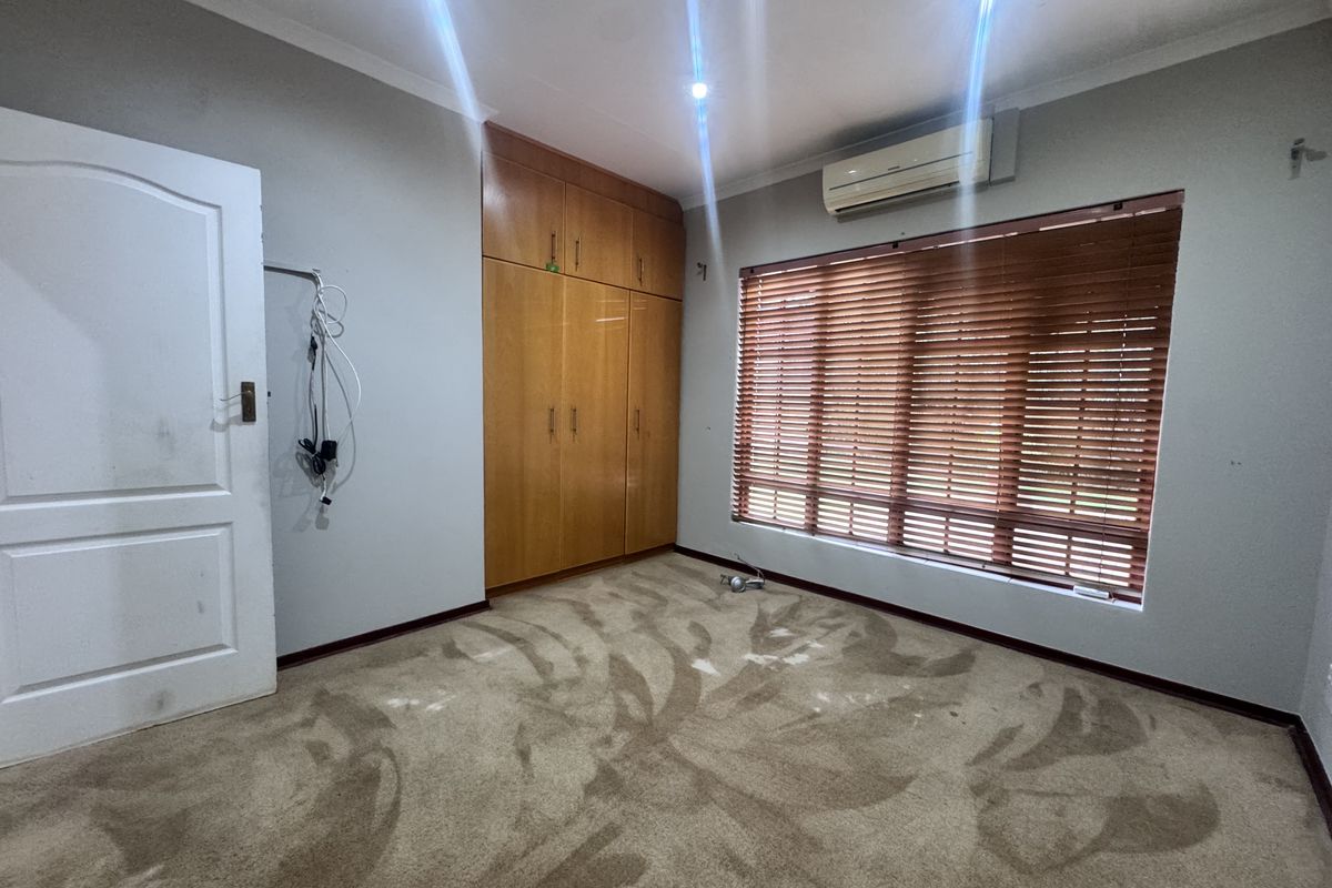 An empty bedroom featuring built-in wooden cupboards, an air conditioning unit, and venetian blinds. The room requires carpet replacement and general cosmetic updates.