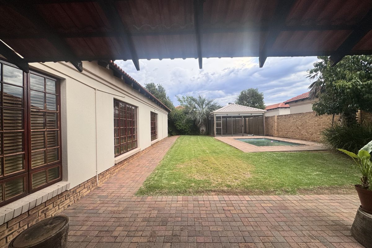 Rear exterior view featuring a covered patio, brick paved area, swimming pool, and a private garden with boundary walling.