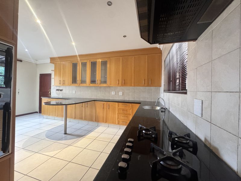 Spacious kitchen featuring wooden cabinetry, granite countertops, a gas hob with extractor fan, and tiled flooring throughout.
