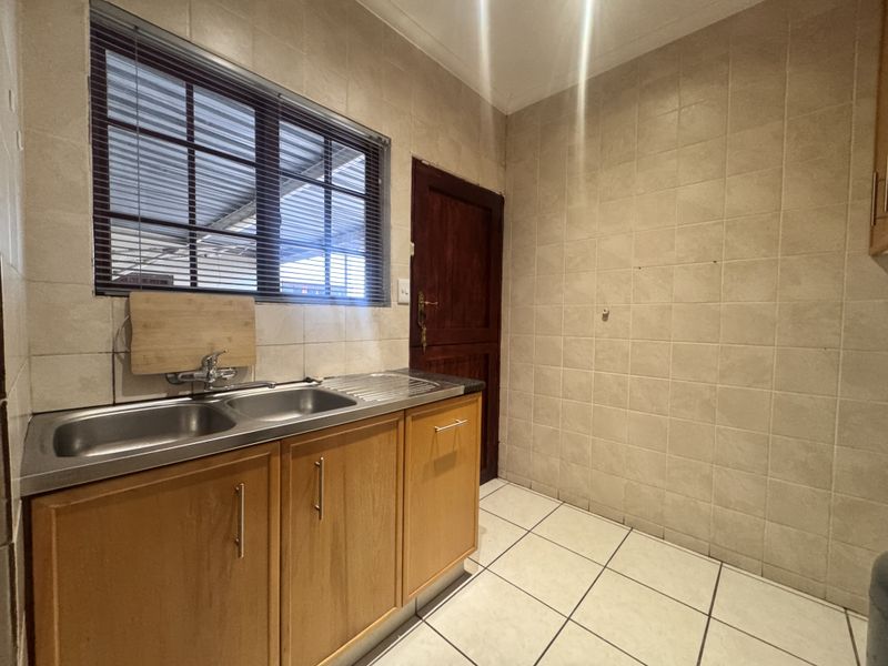 A functional laundry area featuring tiled walls and flooring, a stainless steel double sink, and wooden cabinetry with direct access to an exterior space.