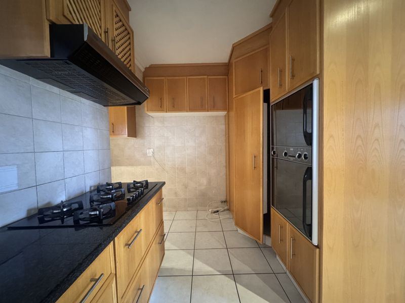 A functional kitchen featuring wooden cabinetry, granite countertops, a gas hob with extractor fan, and a built-in double oven, finished with tiled flooring.