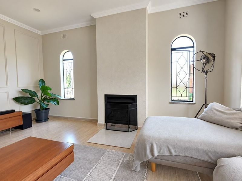 A bright living room featuring a central built-in fireplace, elegant arched windows with leaded glass detailing, and neutral wall finishes.