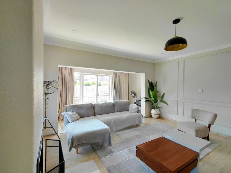 A bright and spacious living room featuring elegant wainscoting, modern pendant lighting, and large sliding glass doors that provide ample natural light.