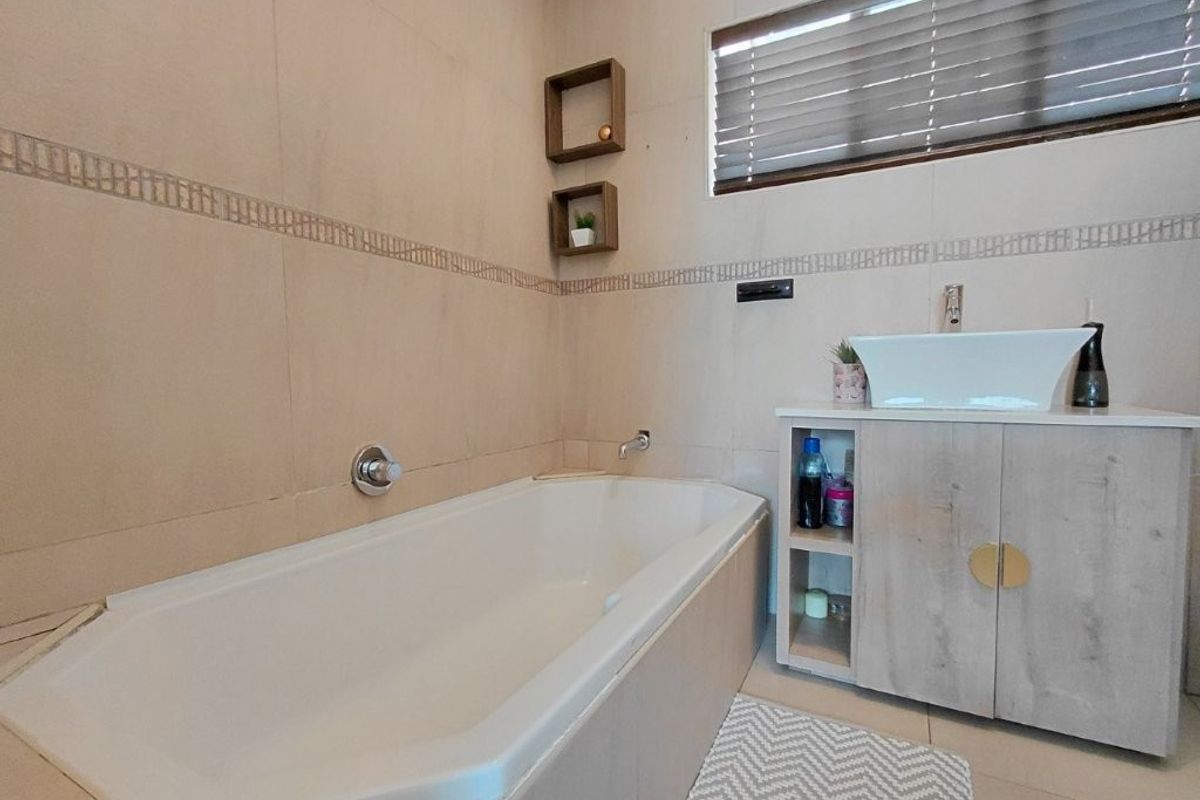 A modern bathroom featuring a built-in bathtub, a vessel sink set on a vanity cabinet, and neutral wall tiling.